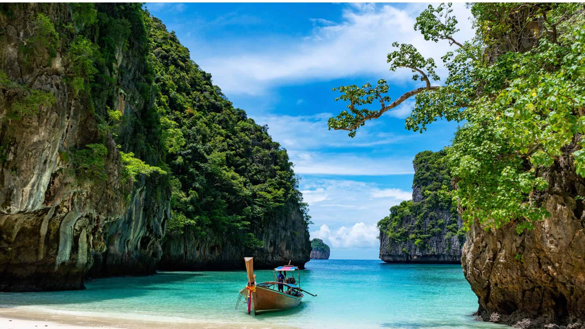beach in thailand, surrounded with mountains and lots of green and in the middle have a small boat in the ocean